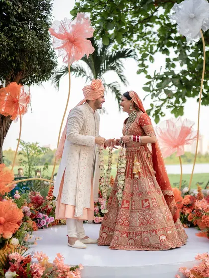 The Varmala exchange amidst a beautiful outdoor setup. This shot captures the couple's happy interaction during a key part of their wedding ceremony.