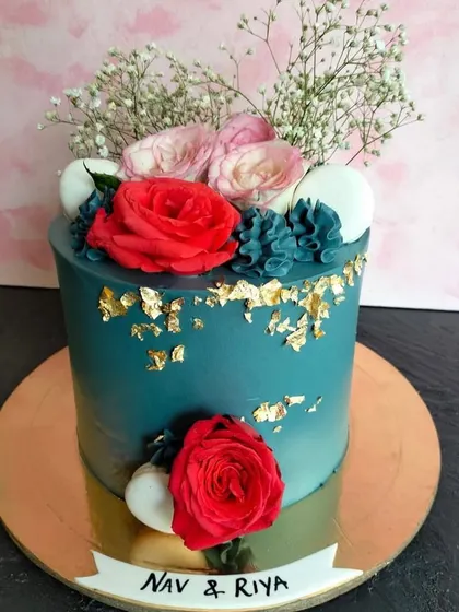 A bold and beautiful teal cake decorated with fresh red roses, macarons, and delicate gold leaf flakes. This design is perfect for making a statement at any celebration.