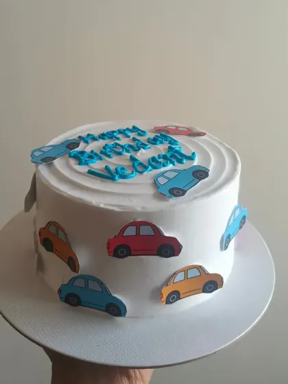 A simple and cute cars theme cake for a little one, with colorful car cutouts decorating the sides and top.