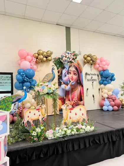 A divine Krishna and Yashoda-themed backdrop for a baby celebration, complete with peacock figures and traditional cow props.