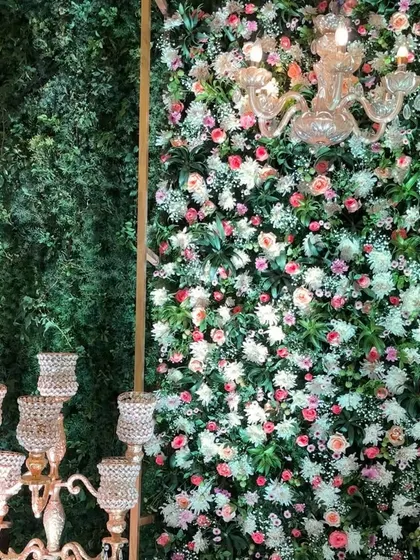 An enchanting photo corner combining a lush green wall with a dense wall of pastel roses and baby's breath. The elegant candelabra and crystal chandelier add a touch of modern romance, perfect for an engagement or reception.