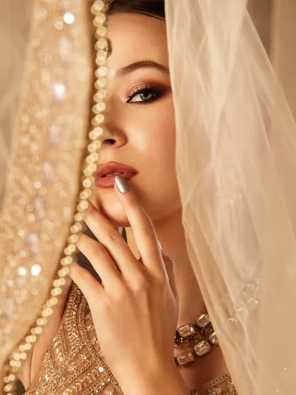 A soft and romantic shot of the bridal look, with the model peeking through a delicate, embroidered veil.