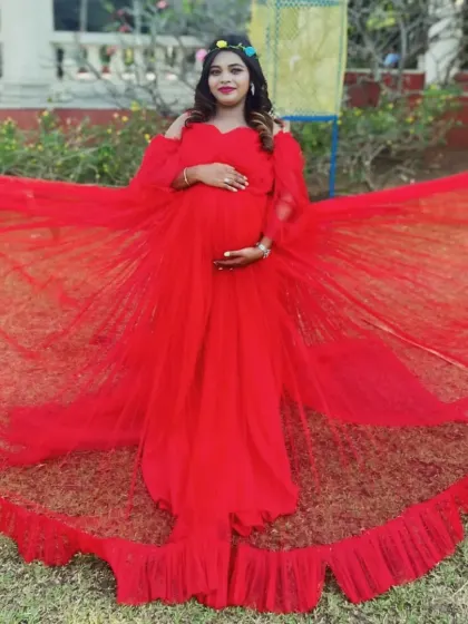 This vibrant red gown features a wide, ruffled trail and off-the-shoulder sleeves, offering a bold and glamorous look for an outdoor maternity shoot.