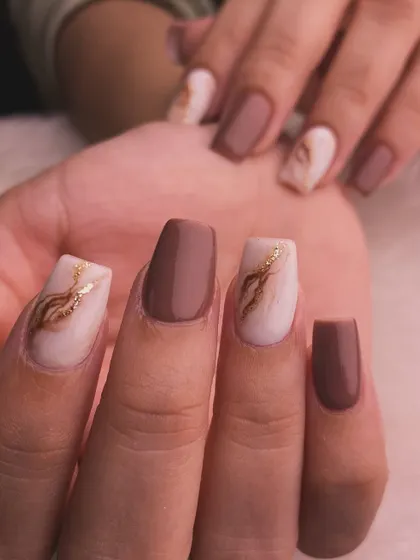 A sophisticated and cozy look with solid brown nails and white marble accent nails featuring a swirl of gold. Perfect for autumn or a coffee lover.