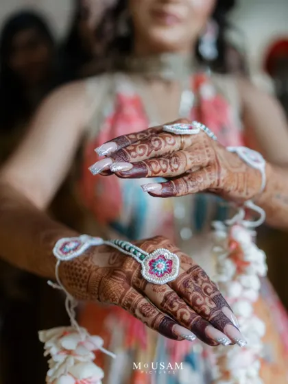 A close-up on the bride's hands, adorned with intricate mehendi and beautiful floral jewelry. These detail shots highlight the traditions and personal style that make each wedding unique.