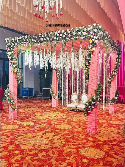 Another angle of the pink and white floral mandap, showing the full structure and the rich patterned carpet.