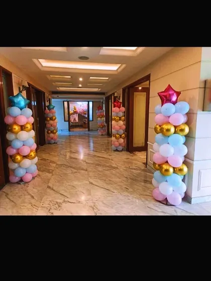 Simple yet elegant balloon pillars in pastel pink, blue, and gold, lining a hallway for a teddy bear-themed event.