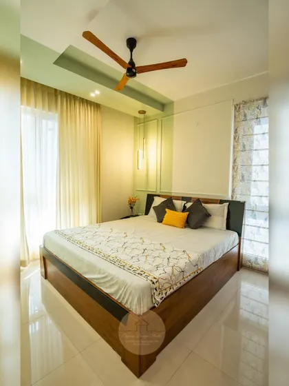A serene guest bedroom with a chic pastel green accent wall. The room features a wooden bed frame, a large wardrobe with fabric-paneled shutters, and elegant pendant lights, creating a calm and welcoming space for visitors.
