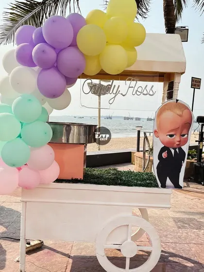 A candy floss cart decorated with pastel balloons and a Boss Baby cutout, perfect for a sweet treat by the sea.