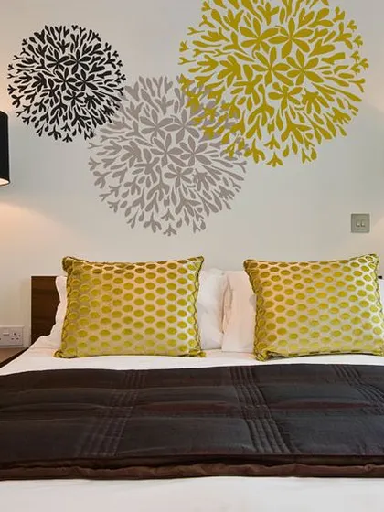 A simple yet effective wallpaper design featuring stylized floral bursts above a bed. It acts as a piece of art, creating a focal point in the room.