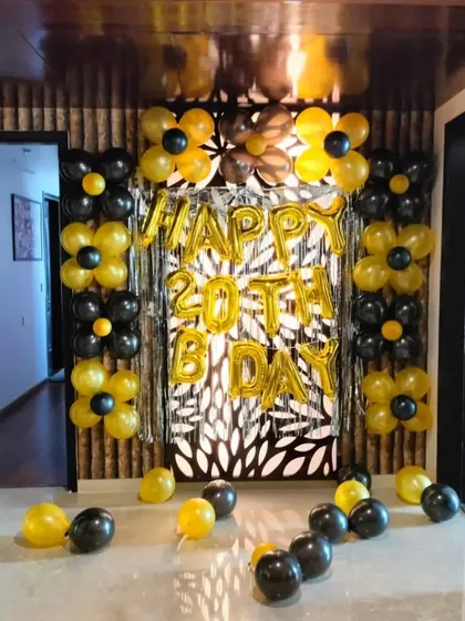 We decorated this entranceway for a 20th birthday party using a black and yellow theme. The setup includes a silver fringe backdrop, "HAPPY 20TH BDAY" foil balloons, and balloon flowers to welcome guests in style.