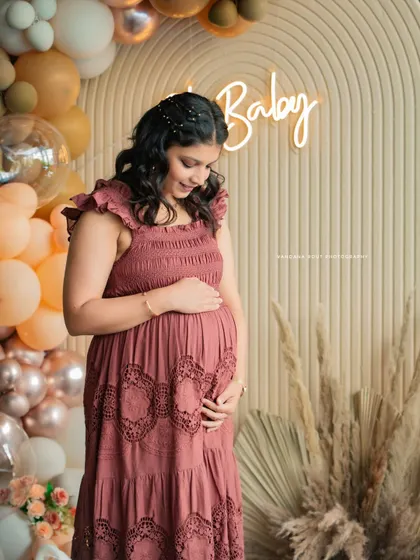 A beautiful solo shot of a mother-to-be at her baby shower, standing before a balloon arch and a neon "Baby" sign.