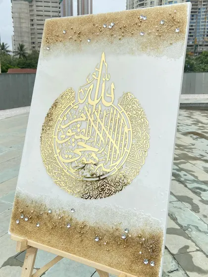 An outdoor shot to capture the natural light on this Ayat al-Kursi artwork. The intricate gold calligraphy is set on a white and sand-colored resin base, with scattered crystals that sparkle in the sun.