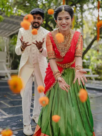 A playful moment during an engagement celebration, with the couple tossing marigold flowers in the air. This captures the fun and festive spirit of the event.