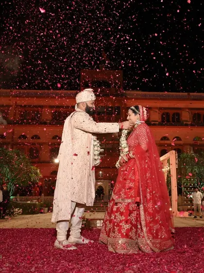 The groom lovingly places the garland around his bride during their royal wedding ceremony, surrounded by a sea of rose petals.