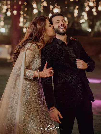 A candid moment of pure joy, as the bride's sister or friend gives the groom a playful kiss on the cheek during a fun-filled event.