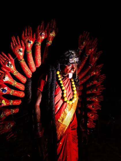 A devotee dressed as the goddess with many arms, a striking and formidable figure in the darkness of the Kulasai festival.