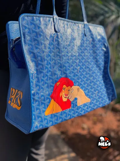 A three-quarter view of the custom Goyard bag, displaying both the main artwork and the side monogram.