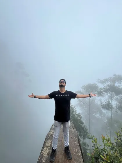 A trekker with arms outstretched at a misty viewpoint in Kodaikanal.