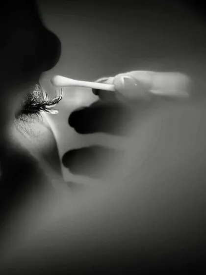 An abstract and artistic close-up in black and white. The focus is on the makeup artist's hand applying mascara, a detail shot that is both intimate and creative.