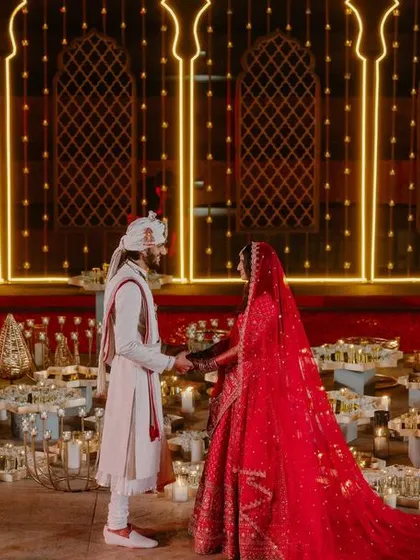 The couple stands against a backdrop of glowing golden arches during their Varmala.