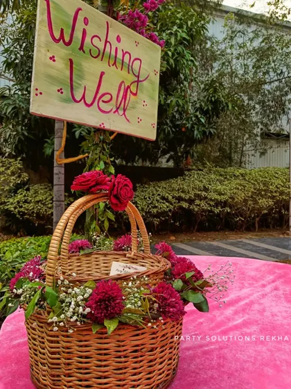 A charming "Wishing Well" corner where guests can leave their blessings for the couple. The hand-painted sign and wicker basket filled with flowers add a rustic and heartfelt touch.