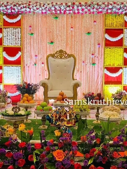 A vibrant and colorful offering display set against a red and yellow backdrop. The foreground is filled with fresh flowers, fruits, and traditional dolls, creating a rich and festive scene.