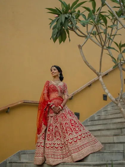 A regal portrait of the couple in their stunning red and cream wedding attire. We use architectural elements like staircases to add a touch of grandeur to our compositions.