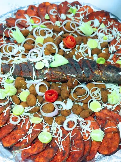 A magnificent seafood platter featuring a whole fried fish, fish finger pieces, and prawn cutlets, garnished with fresh onions and lemon.