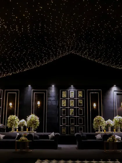 A wide shot of the luxurious lounge area under a canopy of fairy lights. The gallery wall of photos adds a personal touch to the grand, monochrome design.