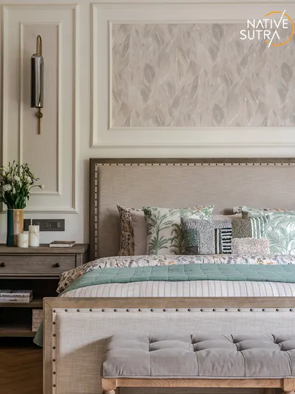 The bed as the undeniable focal point, framed by classic wall mouldings and elegant sconces. The layered bedding with botanical prints and the tufted bench at the foot of the bed create a look of sophisticated comfort.