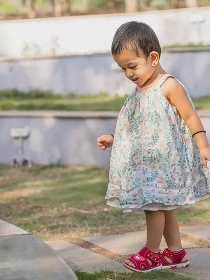 A little girl curiously exploring her surroundings in a sunlit park. This candid photo captures the innocence of childhood as she takes careful steps, completely absorbed in her own little world. These are the quiet, precious moments of a toddler's day.