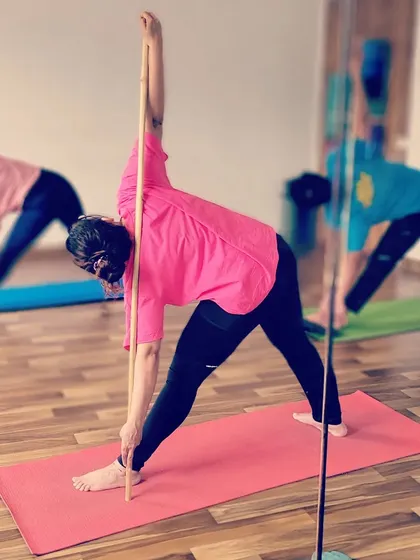 A student practices Trikonasana, or Triangle Pose, with a stick to ensure her spine and arms stay in one long line.