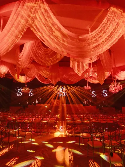 A wide view of the Sangeet hall, with its ceiling of draped fabric, crystal chandeliers, and dramatic stage lighting creating a theatrical atmosphere.