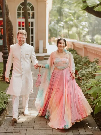 The bride and groom, radiant in their colorful Haldi outfits, walk hand-in-hand through the beautiful gardens of the venue.