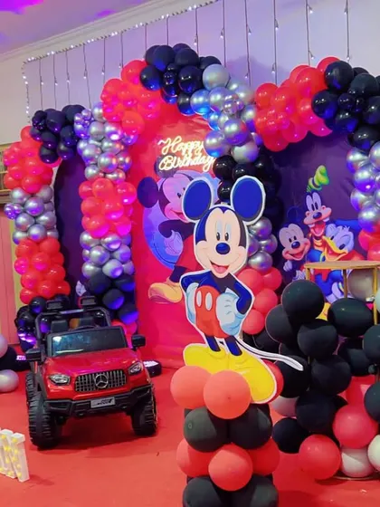 A classic Mickey Mouse Clubhouse birthday party. This grand setup includes a red toy car for the birthday boy's entry, multiple character cutouts, and balloon arches in Mickey's signature colors.