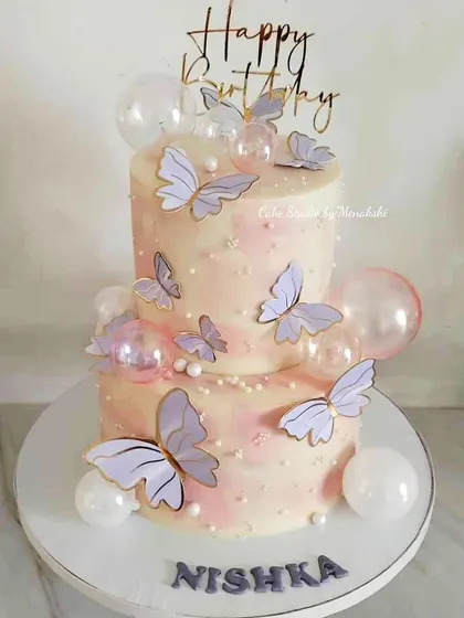A pretty two-tier pink birthday cake decorated with delicate butterflies and translucent bubbles. This entire creation is made without fondant, using buttercream to create a soft, dreamy texture.