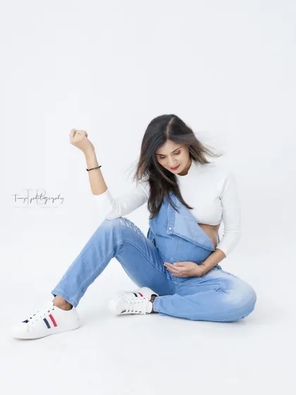 A fun and casual solo shot. The mom-to-be is all smiles in denim overalls and sneakers, creating a playful and relaxed vibe.