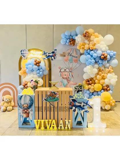 Vivaan's first birthday took flight with this adorable hot air balloon and airplane theme. The setup includes a cute teddy bear pilot, a large light-up number "1", and a soft blue and yellow color palette.