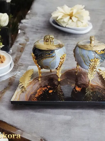 A modern and luxurious dry fruit gift set, featuring two marble-finish jars with ornate golden leaf stands on a matching tray. This is a contemporary take on traditional festive gifting, perfect for impressing discerning clients.