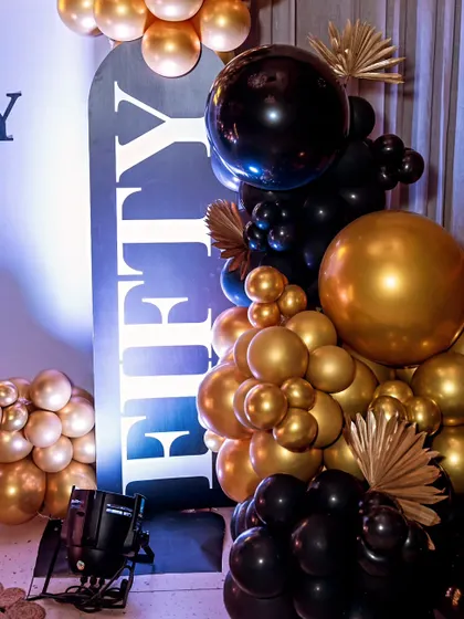 A detail shot of the black and gold 50th birthday decor. The contrast of the matte black 'FIFTY' sign against the metallic gold balloons is bold and stylish.