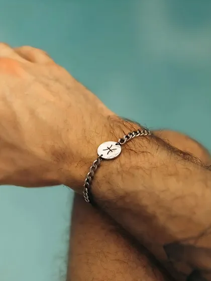 A man wearing my silver chain-link bracelet featuring a custom-engraved disc with the Pisces zodiac symbol. This style offers a modern alternative to the classic cuff.