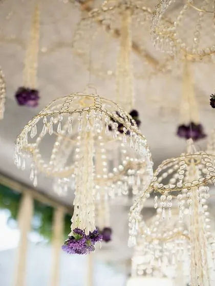 Delicate floral chandeliers made of jasmine and crystal beads, with a pop of purple from fresh orchids, hang from the ceiling.