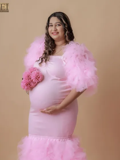 A lovely portrait of a mom-to-be in a pink ruffled gown, holding a matching pink floral prop.