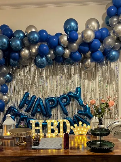 This tabletop birthday decoration is perfect for smaller spaces or as a main feature on the gift table. It includes a silver shimmer curtain, a blue and silver balloon garland, and light-up "HBD" letters.