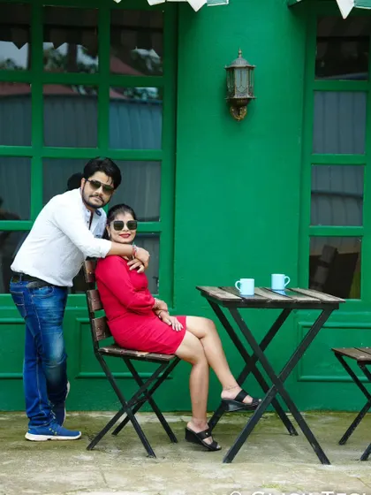 A cool and casual pose at an outdoor cafe set, with a vibrant green wall in the background.