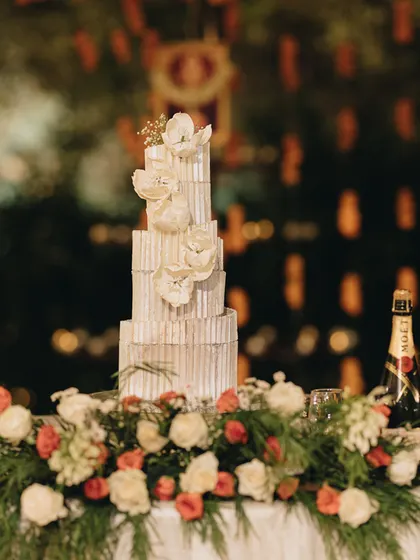 An exquisite art-deco inspired wedding cake, standing as a centerpiece of the dessert table, surrounded by fresh flowers.