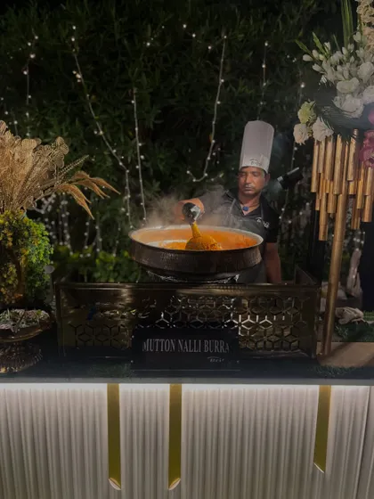 A chef serves a steaming portion of Mutton Nalli Burra at a beautifully decorated live station.