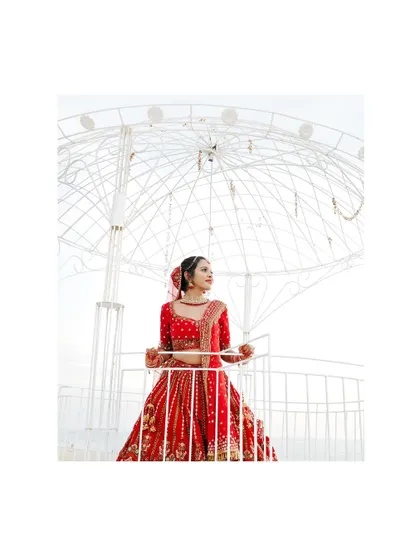 A beautiful bride in her red lehenga, posing under a large white umbrella structure, looking like a princess.