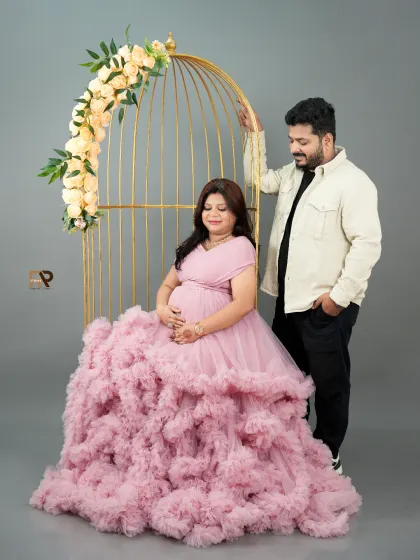 A portrait of pure elegance. The mom-to-be is seated in our popular golden birdcage prop, wearing a soft pink ruffled gown that cascades around her. This setup is perfect for creating a romantic and sophisticated look.